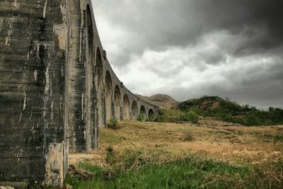 Railway bridge by field against cloudy sky