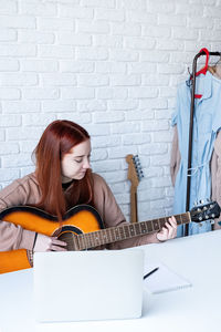 Portrait of young woman playing guitar against brick wall