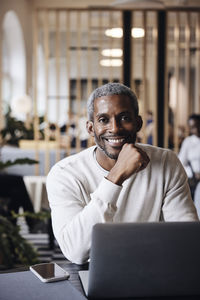 Portrait of smiling male business professional sitting with laptop at office