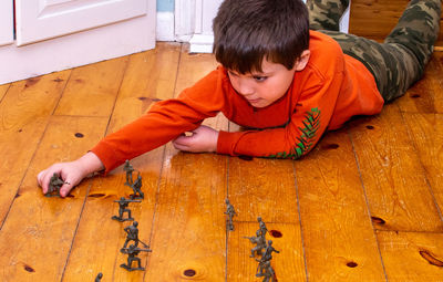 Young boy with plastic soldiers playing war on the hard wood floor