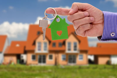 Cropped hand of man holding key ring against house