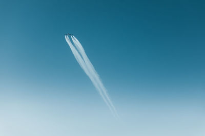 Low angle view of airplane flying with vapor trails in clear blue sky
