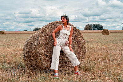 Full length of young woman standing by hay on field
