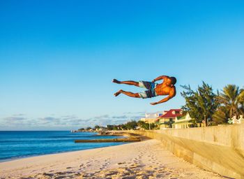 Man jumping over sea against clear blue sky