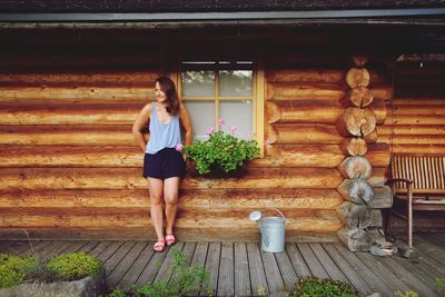 Full length of woman standing against log cabin