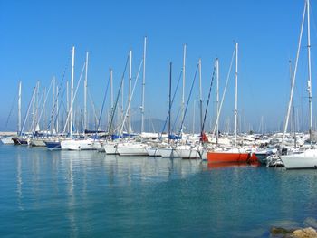 Boats moored in calm sea against clear blue sky