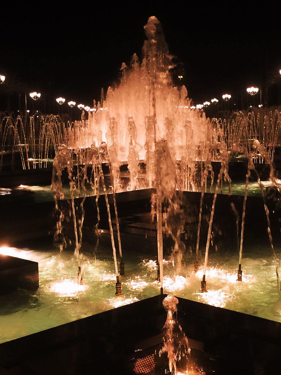 night, water, illuminated, built structure, architecture, building exterior, wet, splashing, reflection, motion, season, fountain, outdoors, cold temperature, city, winter, weather, incidental people, pier