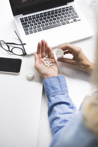 Cropped hand of businesswoman taking medicines while sitting at office