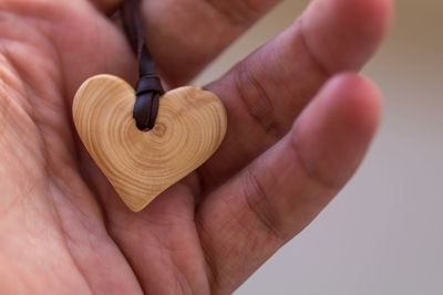 Cropped hand of person holding wooden heart shape locket