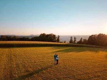 Couple standing on field against clear sky during sunny day