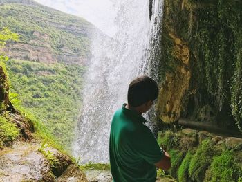 Rear view of man looking at waterfall in forest