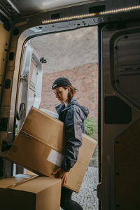 Side view of female delivery person unloading box from van trunk