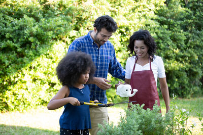 Girl with gardening equipment while parents holding watering can in yard
