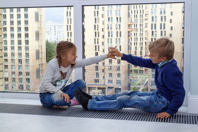 Happy friends sitting on floor against buildings