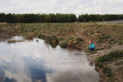 Child playing with a stick in the water in a park on a cloudy day