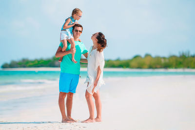 Full length of couple holding hands at beach against sky