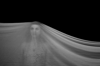 Woman covered with fabric against black background