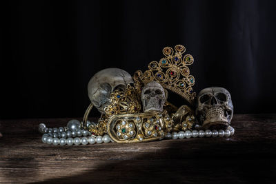 Close-up of human skulls and gold jewelry on table against black background