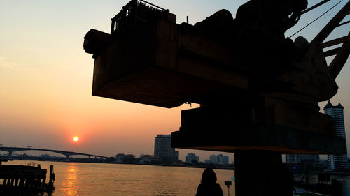 Silhouette buildings by sea against sky during sunset