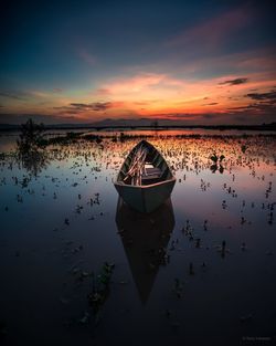 Boat moored in lake against sky during sunset