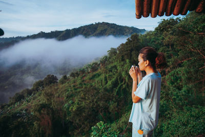 Side view of young woman standing against mountain