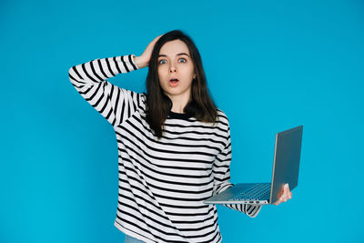 Portrait of young woman standing against blue background