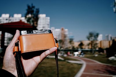 Midsection of person holding umbrella in city against sky