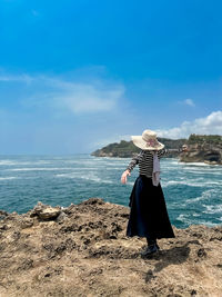 Side view of woman standing at beach against blue sky