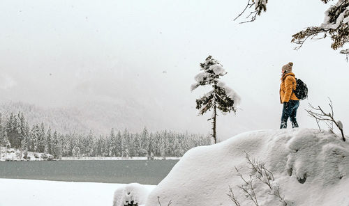 Rear view of person in winter clothes standing on shore of frozen lake.