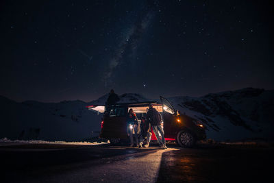 People with illuminated van against sky at night