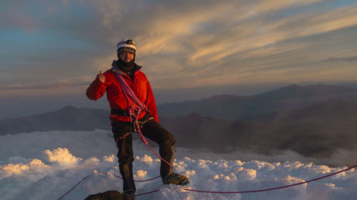 Male climber standing on the summit of cotopaxi volcano wearing red coat  during a cloudy sunrise