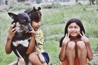 Girl holding dog while sitting with female friend on field