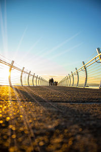 People on road against clear sky during sunset