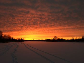 Snow covered landscape against sky during sunset