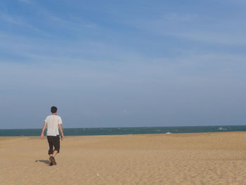 Full length rear view of boy walking at beach against sky