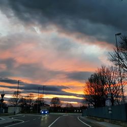 Road by silhouette trees against dramatic sky during sunset