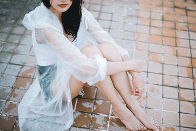 Low section of woman in raincoat sitting on paving stone