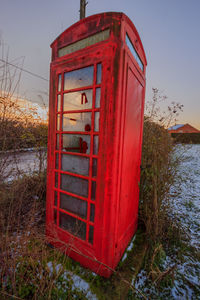 Red telephone booth on field against sky