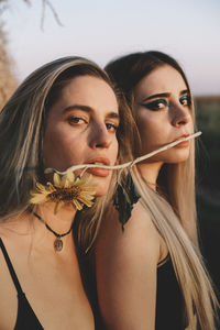 Close-up portrait of beautiful women biting flower while standing outdoors