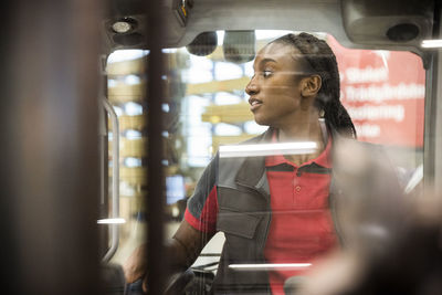 Female warehouse worker looking away while sitting in forklift seen through windshield