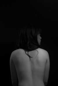 Rear view of shirtless woman standing against black background