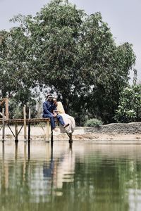 People sitting by lake against trees