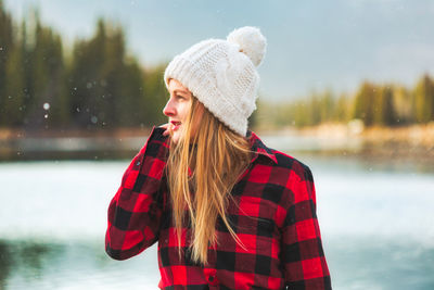 Smiling woman looking away while standing by lake during winter