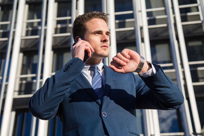 Low angle view of businessman talking on smart phone while standing against building