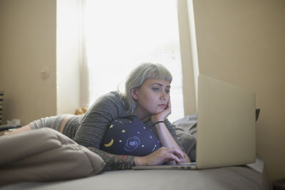 Young woman lying in bed looking at laptop