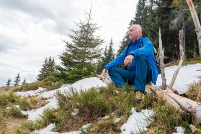 Low angle view of man sitting on rock against sky