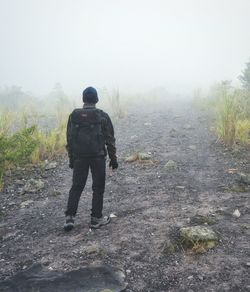 Rear view of man walking on landscape in foggy weather