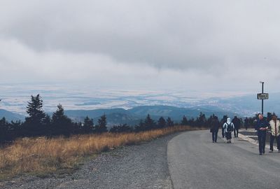 Rear view of people walking on road along landscape