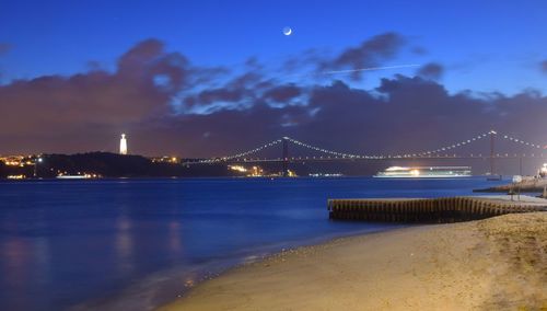 Illuminated bridge over river with city in background