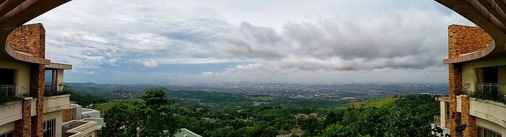 Panoramic shot of house surrounded by trees against cloudy sky